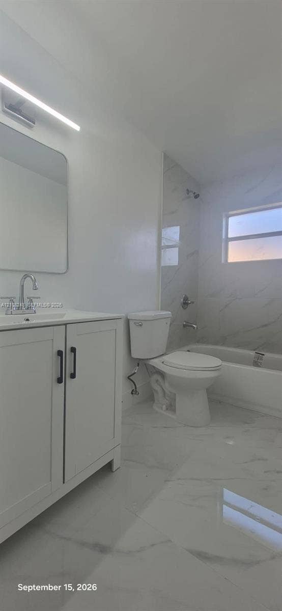 4490 Pine Garden Lane, Lake Worth, FL 33467 Bathroom featuring a white vanity cabinet with matte black hardware, stone-finish tile flooring, tub-shower combination with floor-to-ceiling tile surround, and an integrated LED vanity light