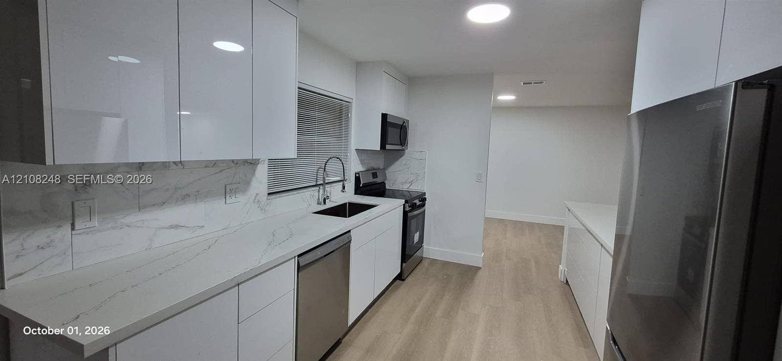 4490 Pine Garden Lane, Lake Worth, FL 33467 Kitchen featuring high-gloss white cabinetry, stone-finish countertops with matching backsplash, stainless steel appliances, and wood-finish flooring