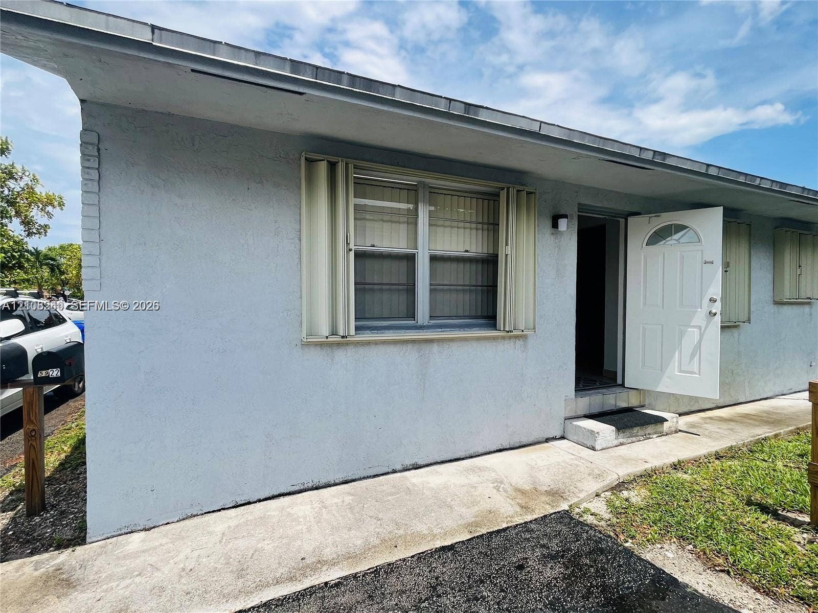 Single-story exterior featuring light-colored stucco siding, metal accordion hurricane shutters, and a covered entry with a glass-insert door