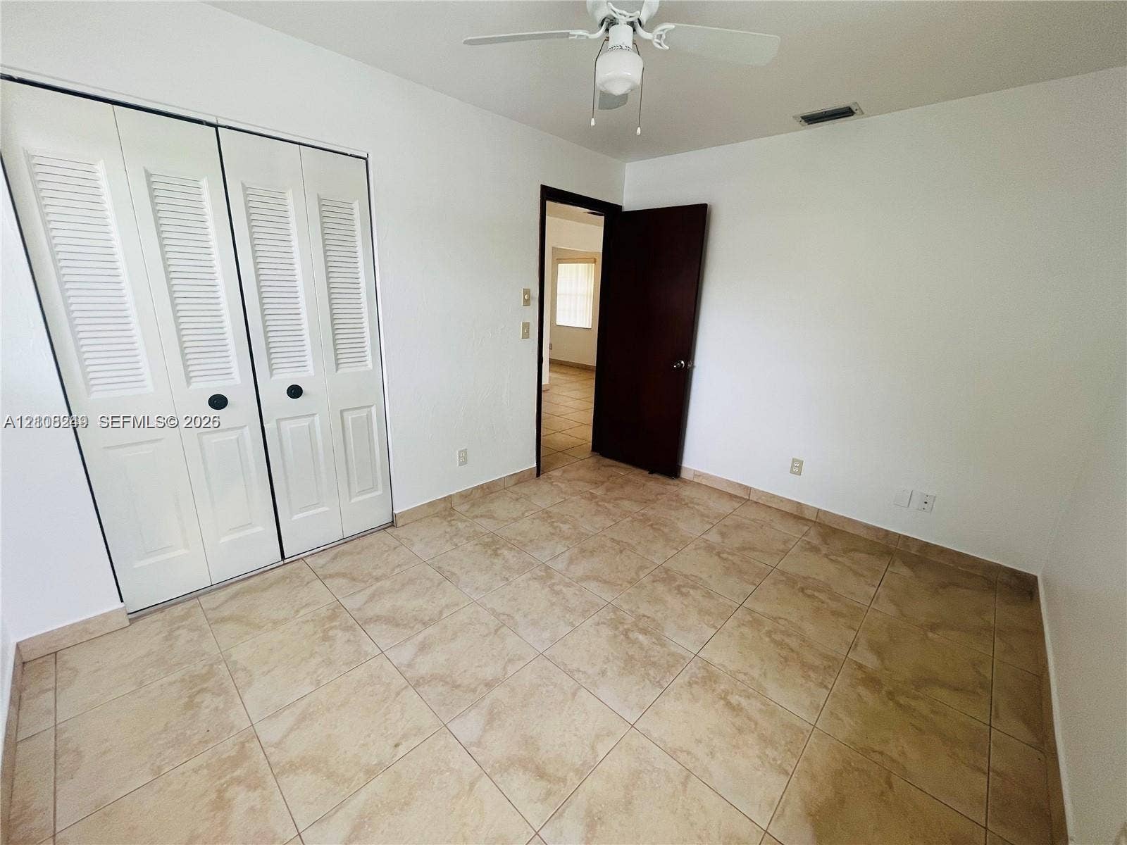 Neutral-tone tile flooring, white bi-fold closet doors, and ceiling-mounted fan with integrated light fixture