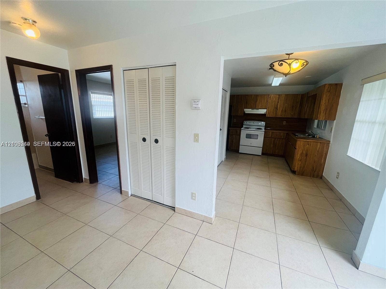 Kitchen featuring wood-finish cabinetry, tile flooring, and overhead lighting, complemented by a hallway with louvered-panel closet doors and dark-finish interior door frames