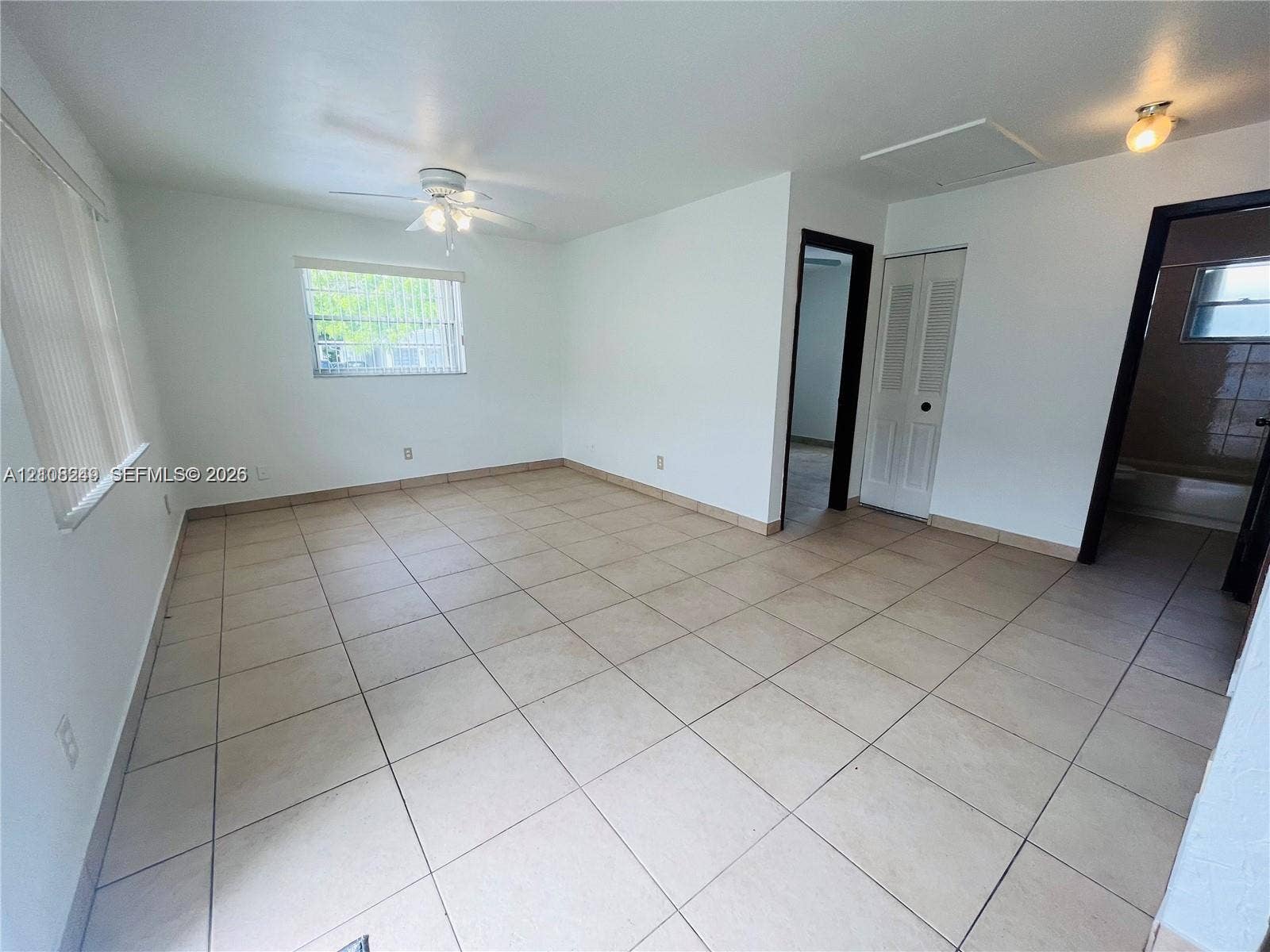 Neutral interior space featuring large-format ceramic tile flooring, a ceiling fan with integrated lighting, and louvered closet doors