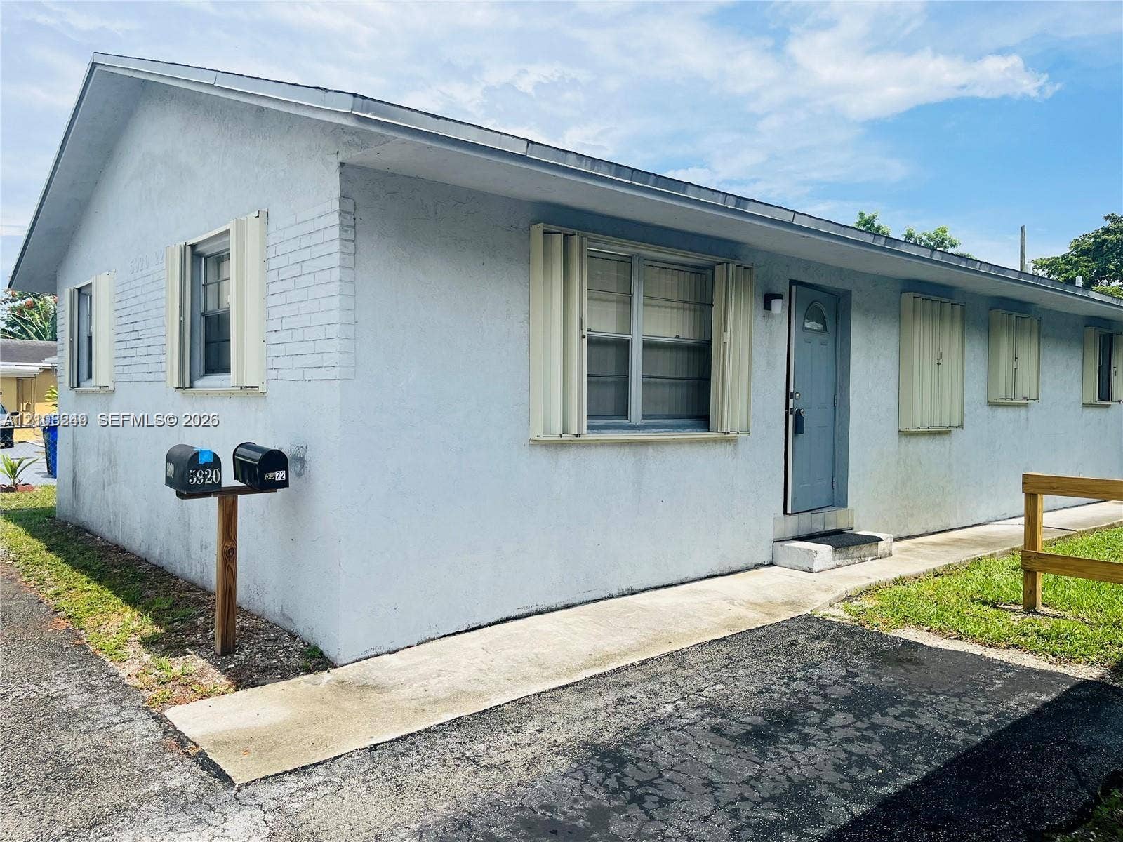Stucco exterior featuring accordion hurricane shutters, a concrete walkway, and paved surface area