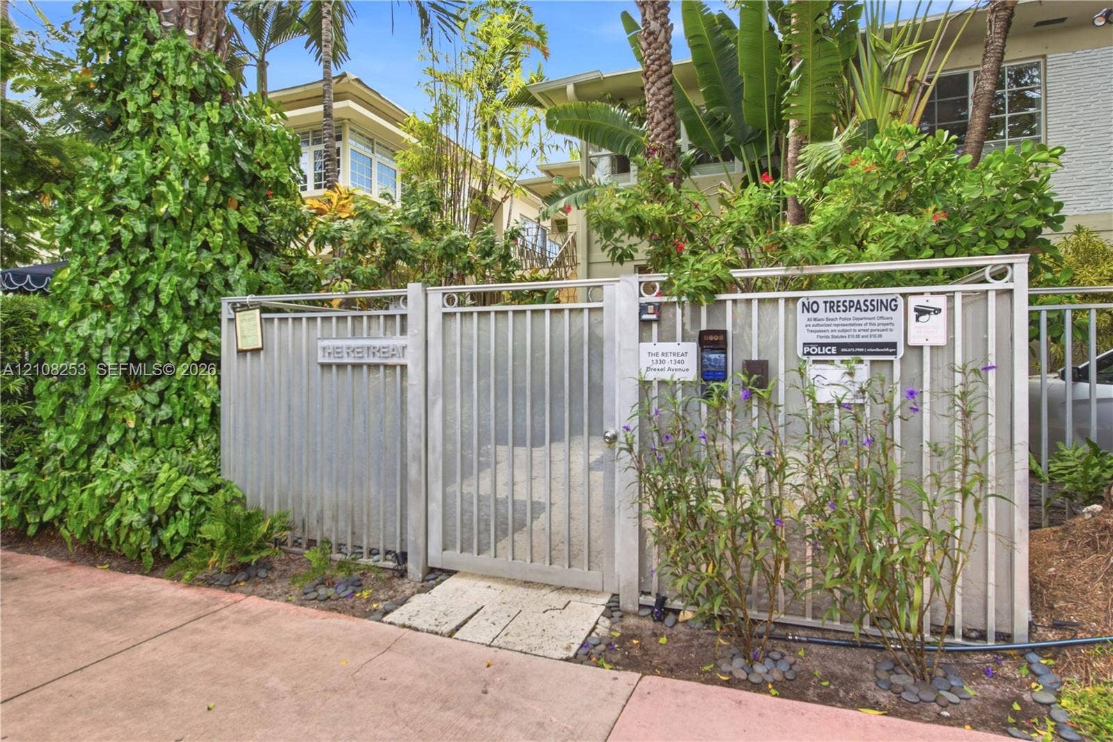 1330 Drexel Avenue, #102, Miami Beach, FL 33139 Gated entrance featuring metallic fencing, a secure access keypad, and established tropical landscaping