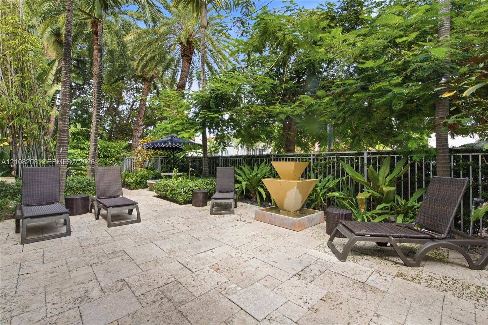 1330 Drexel Avenue, #102, Miami Beach, FL 33139 Stone paver patio featuring a tiered fountain, metal perimeter fencing, and mature landscaping