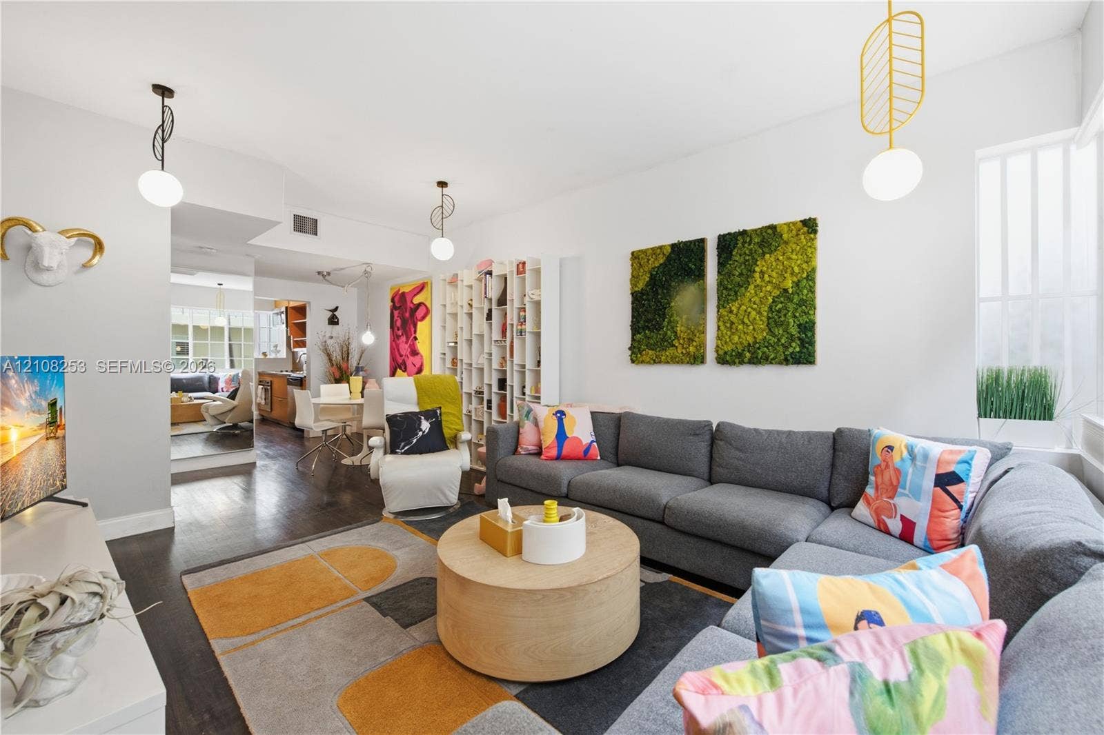 1330 Drexel Avenue, #102, Miami Beach, FL 33139 Living area featuring wood-finish flooring, floor-to-ceiling built-in shelving, and custom pendant light fixtures