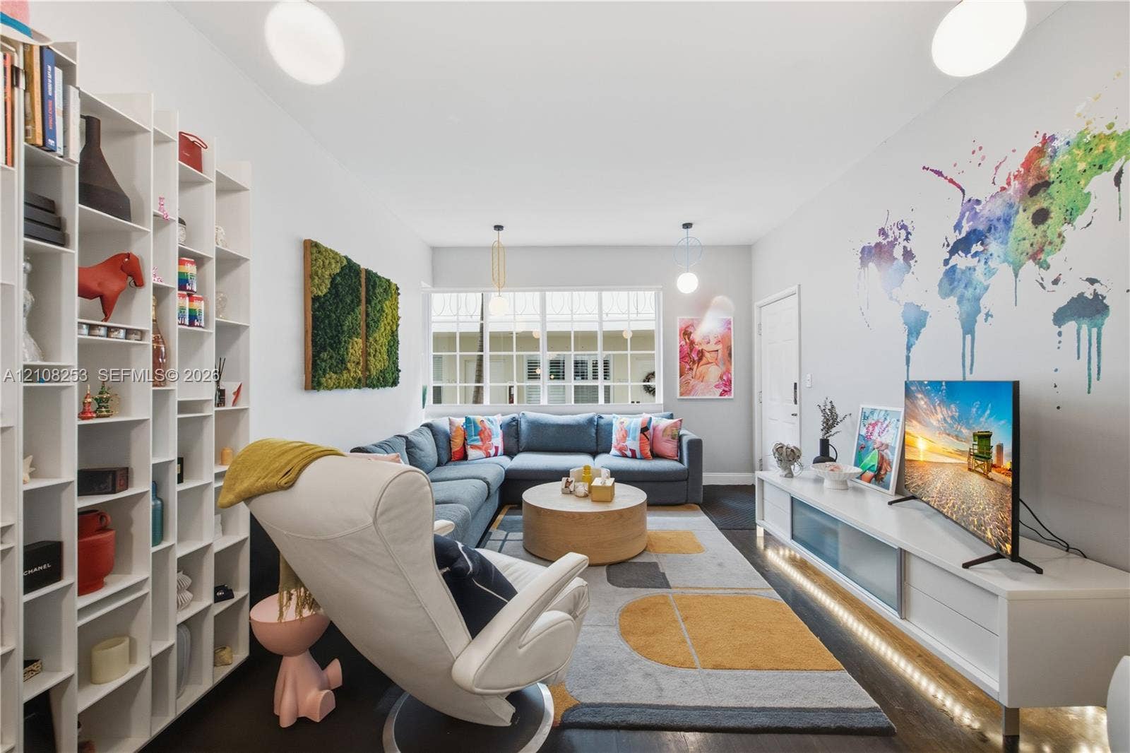 1330 Drexel Avenue, #102, Miami Beach, FL 33139 Floor-to-ceiling white built-in shelving, multi-pane window, integrated low-profile media cabinetry with under-cabinet lighting, and dark-finish flooring