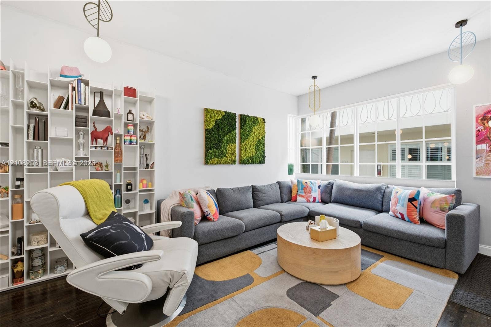 1330 Drexel Avenue, #102, Miami Beach, FL 33139 Built-in floor-to-ceiling shelving, large multi-pane window with decorative muntins, dark-finish flooring, and minimalist pendant lighting