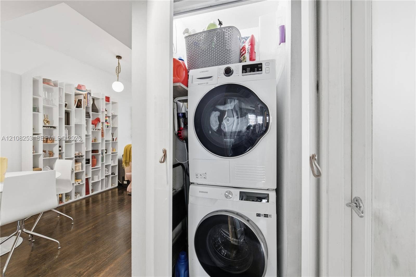 1330 Drexel Avenue, #102, Miami Beach, FL 33139 Stacked laundry center featuring a front-load washer and dryer set, white built-in shelving, and wood-finish flooring