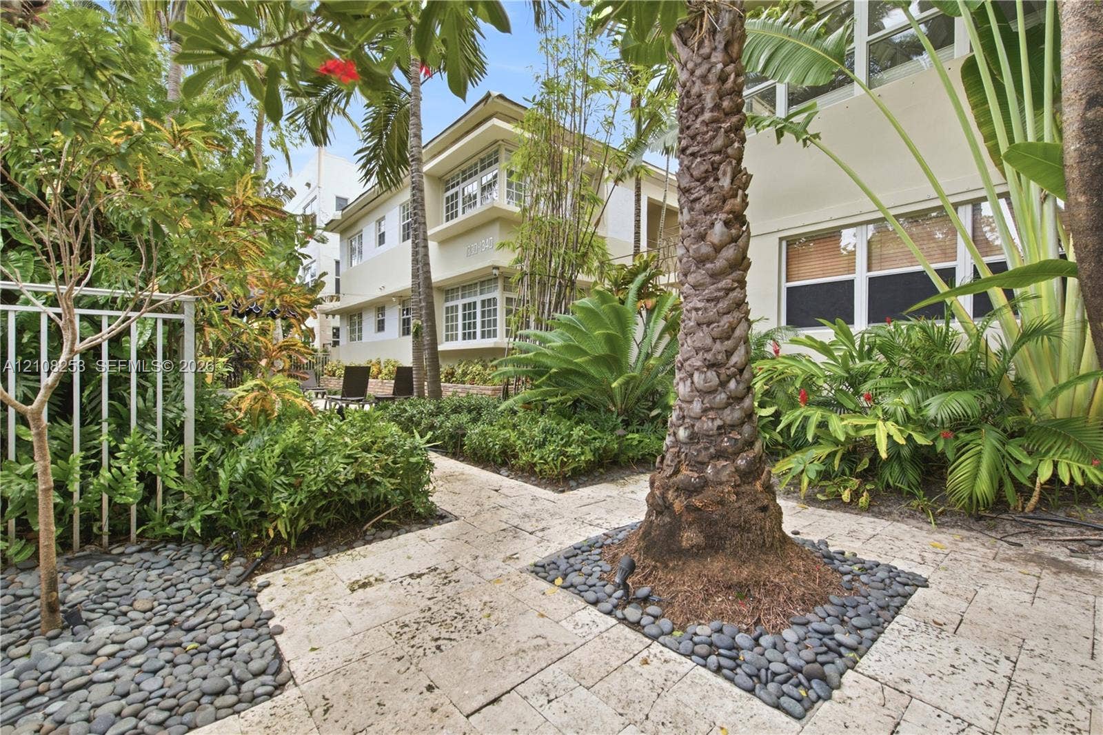 1330 Drexel Avenue, #102, Miami Beach, FL 33139 Landscaped courtyard featuring stone paver walkways, decorative pebble borders, mature palm trees, and lush tropical greenery