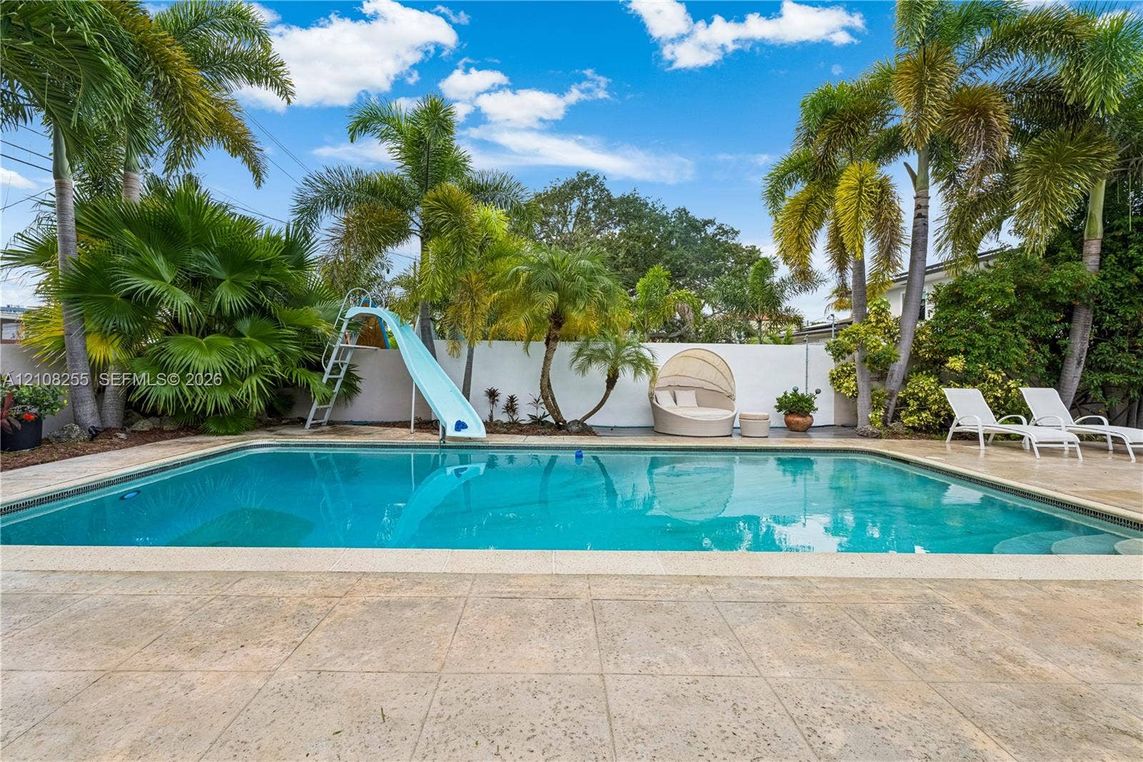 1650 NE 171st Street, North Miami Beach, North Miami Beach, FL 33162 In-ground swimming pool featuring a built-in slide, surrounded by a paved deck and mature palm trees enclosed by a privacy wall