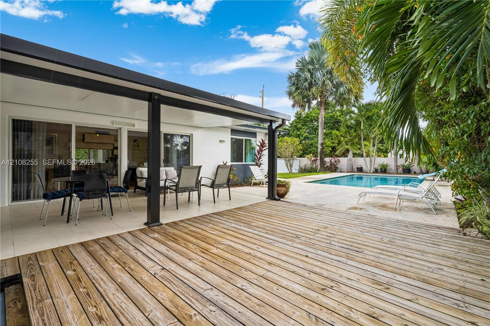 1650 NE 171st Street, North Miami Beach, North Miami Beach, FL 33162 Covered patio featuring a wood-plank deck, tile flooring, sliding glass doors, and a swimming pool with a stone pool deck