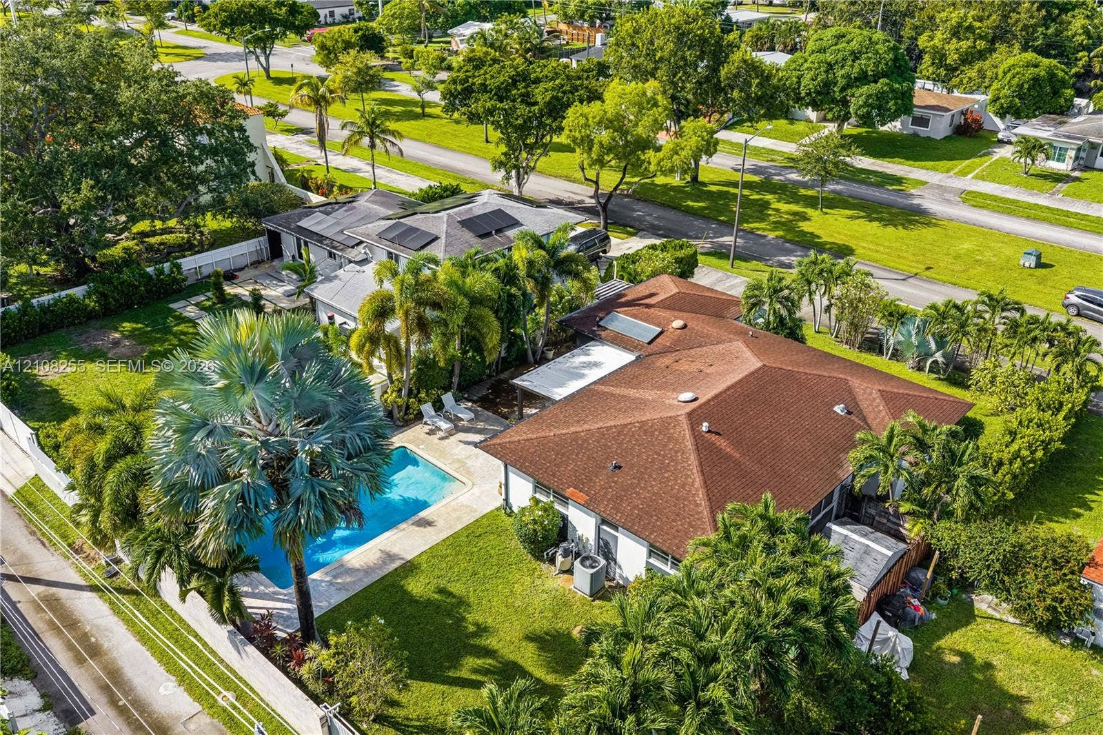 1650 NE 171st Street, North Miami Beach, North Miami Beach, FL 33162 Aerial perspective of a property featuring an in-ground swimming pool, a patio area with a pergola, roof-mounted solar panels, and mature palm landscaping