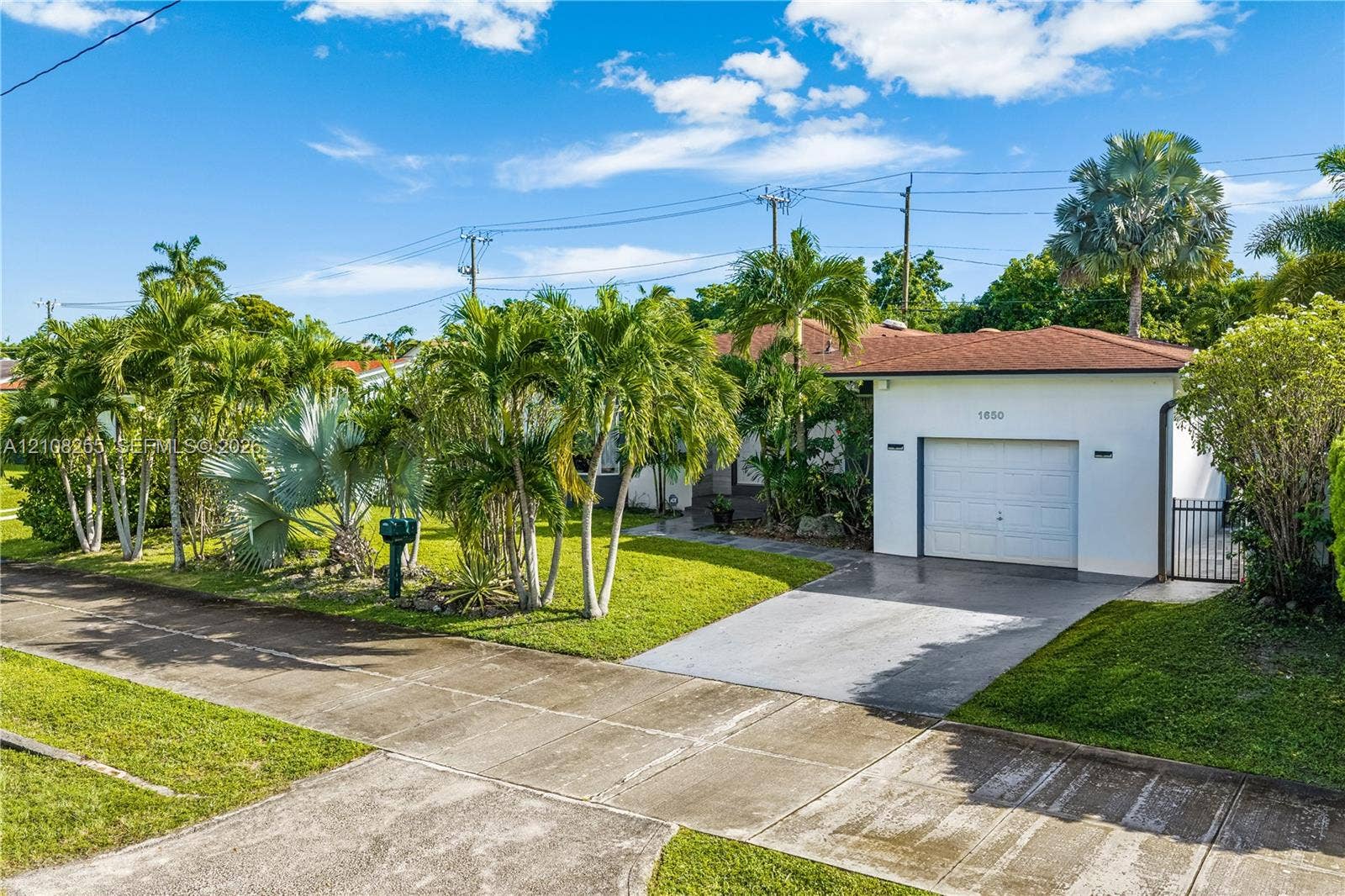 1650 NE 171st Street, North Miami Beach, North Miami Beach, FL 33162 Single-story stucco exterior featuring a concrete driveway, attached garage, shingle roof, and mature palm landscaping