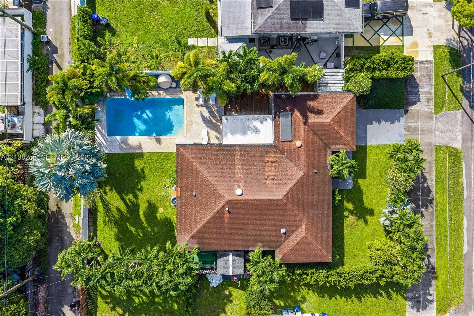 1650 NE 171st Street, North Miami Beach, North Miami Beach, FL 33162 Aerial perspective featuring a shingled roof, an inground swimming pool, paved patio areas, and manicured landscaping with mature palm trees