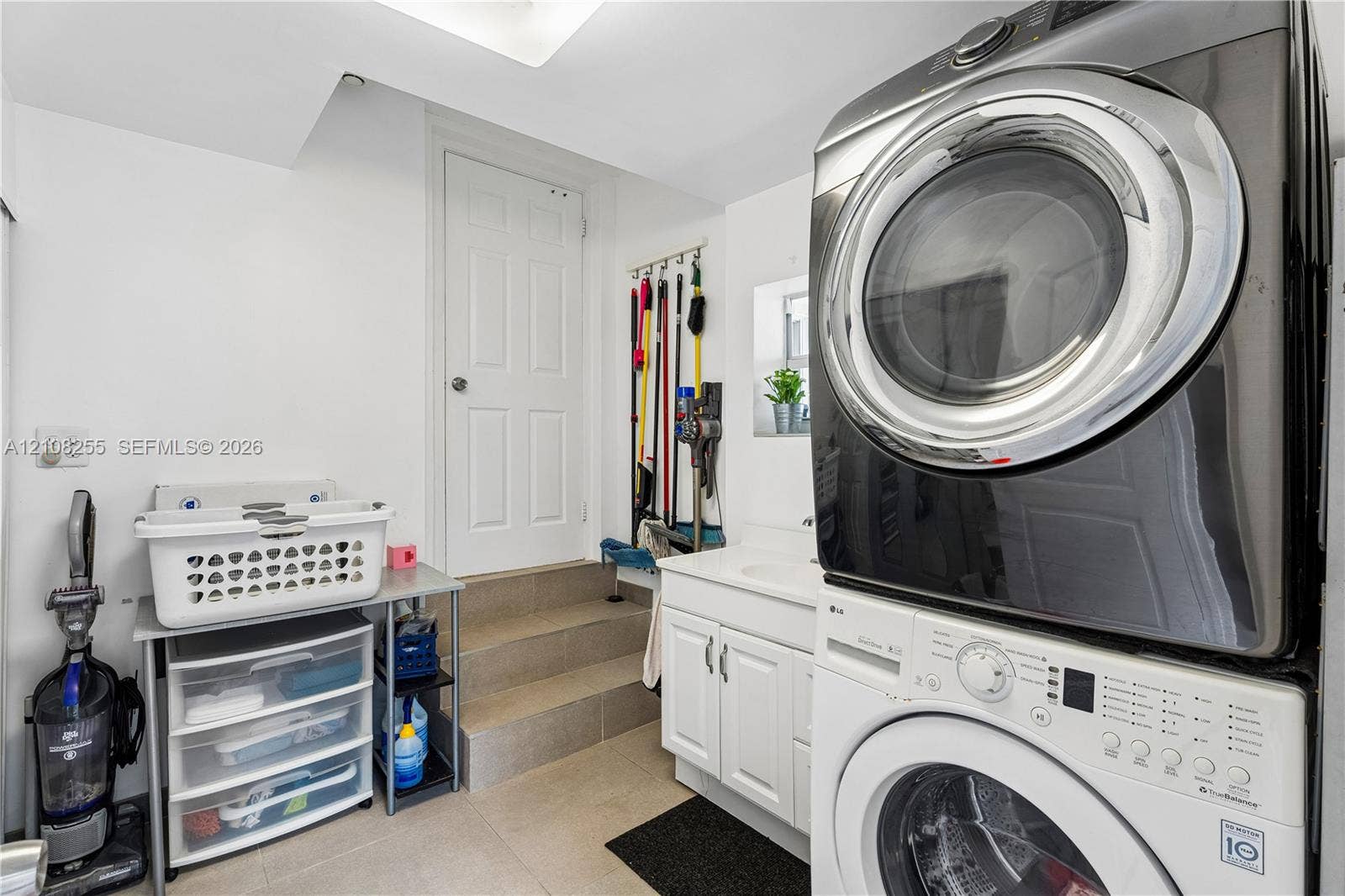 1650 NE 171st Street, North Miami Beach, North Miami Beach, FL 33162 Laundry area featuring a stacked washer and dryer, white shaker-style cabinetry, an integrated basin sink, and tiled flooring