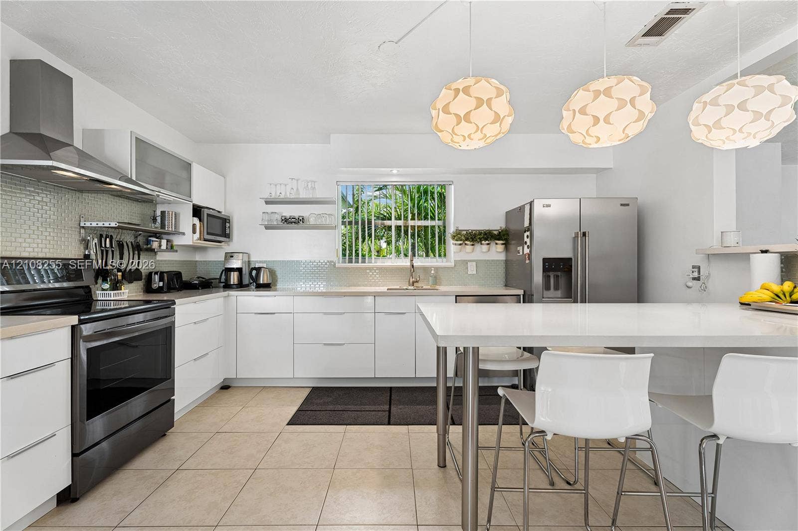 1650 NE 171st Street, North Miami Beach, North Miami Beach, FL 33162 Kitchen featuring white flat-panel cabinetry, stainless steel appliances, a tile backsplash, and a central island with a solid-surface countertop
