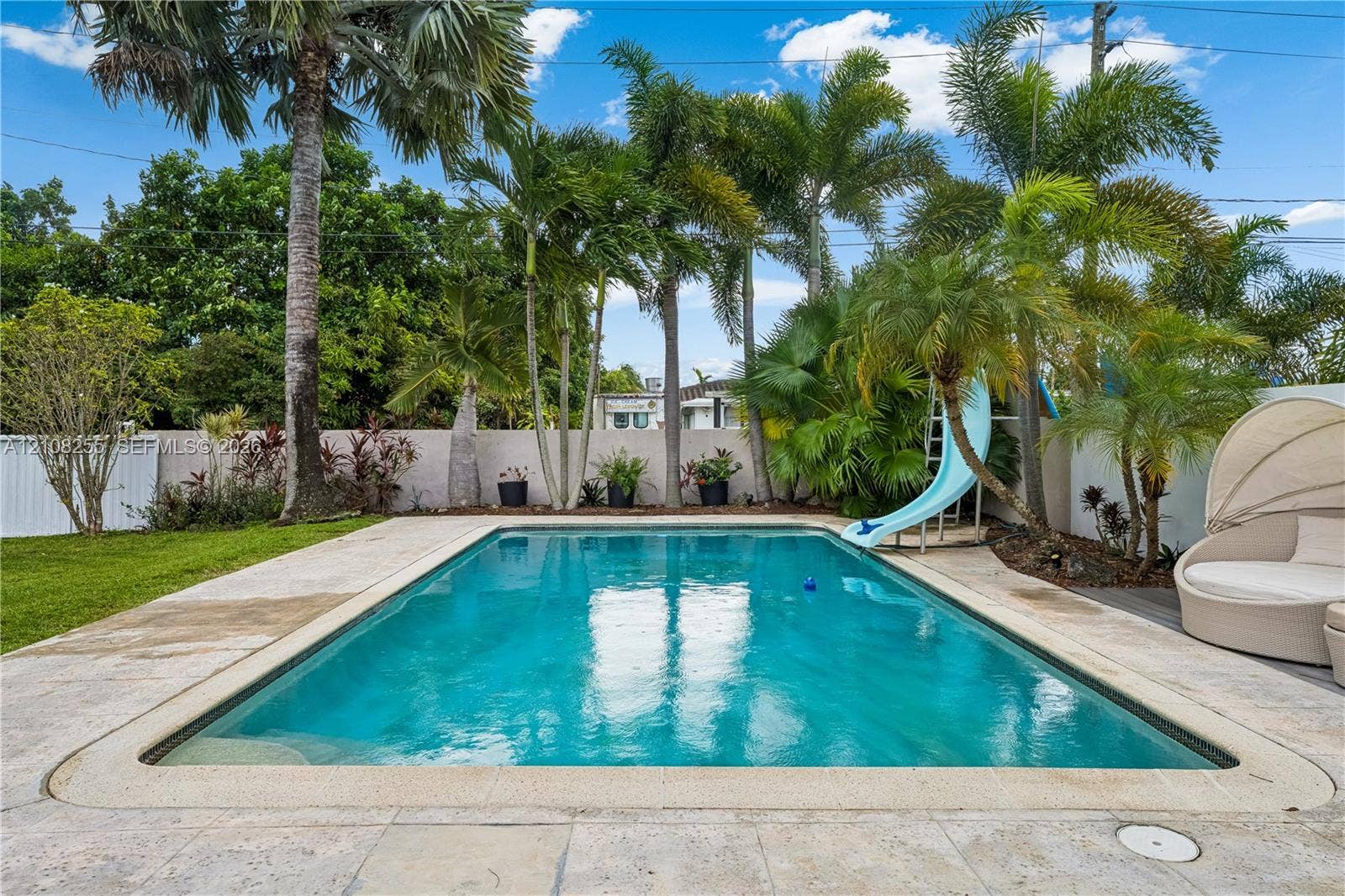 1650 NE 171st Street, North Miami Beach, North Miami Beach, FL 33162 In-ground swimming pool featuring a built-in slide, surrounded by stone paver decking, privacy wall, and mature palm trees