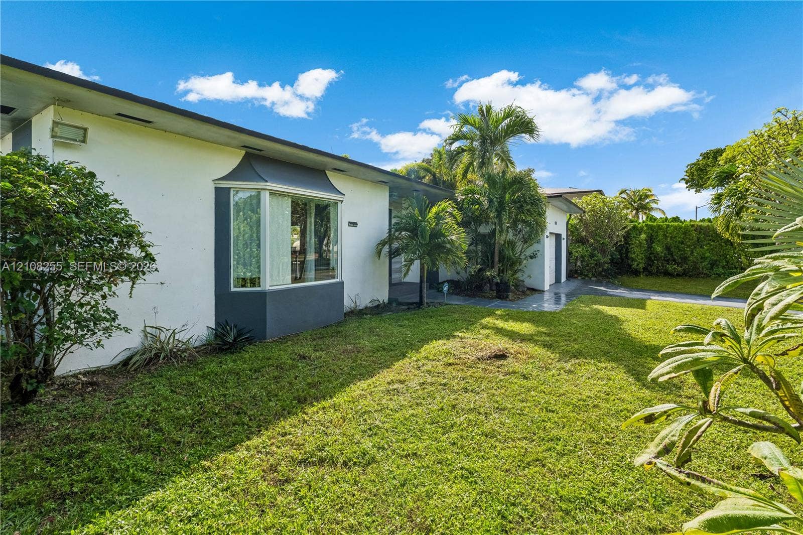 1650 NE 171st Street, North Miami Beach, North Miami Beach, FL 33162 Single-story exterior featuring white stucco siding, a charcoal-trimmed bay window, mature palms, and expansive lawn