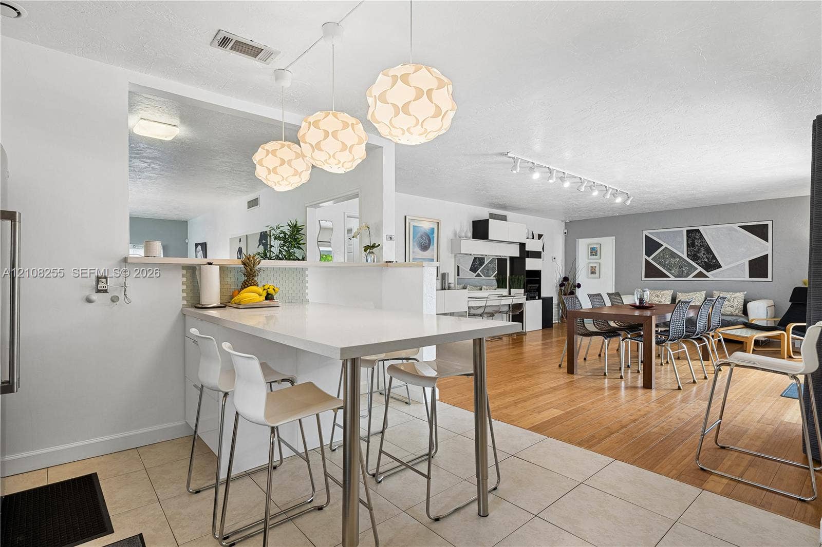 1650 NE 171st Street, North Miami Beach, North Miami Beach, FL 33162 Kitchen peninsula with a solid-surface countertop and integrated breakfast bar, complemented by three spherical pendant light fixtures, large-format tile flooring, and wood-finish flooring