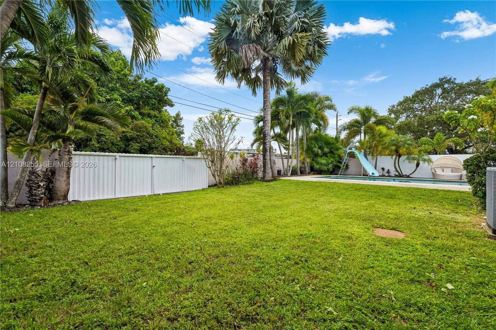 1650 NE 171st Street, North Miami Beach, North Miami Beach, FL 33162 Fenced backyard featuring a manicured lawn, palm trees, an in-ground pool with a built-in slide, and privacy wall enclosure