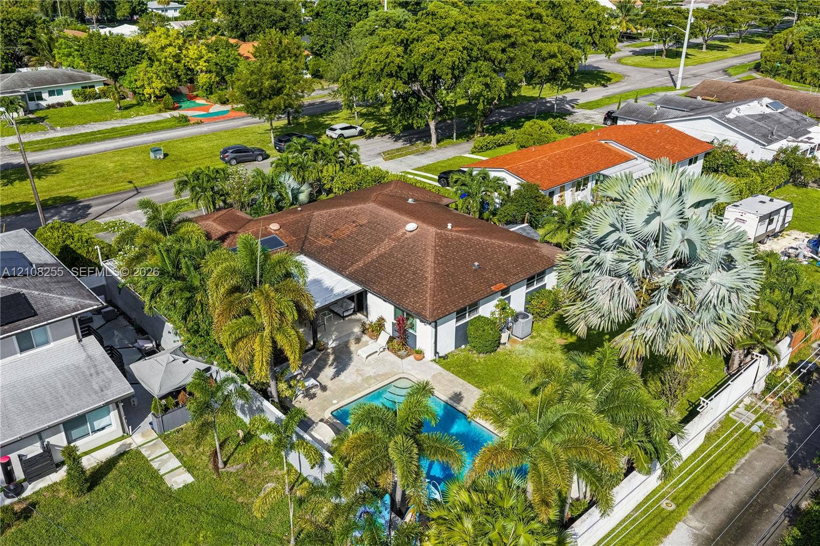 1650 NE 171st Street, North Miami Beach, North Miami Beach, FL 33162 Aerial perspective featuring a shingle-roof residence, an in-ground swimming pool, a concrete patio, established palm trees, and a fenced perimeter
