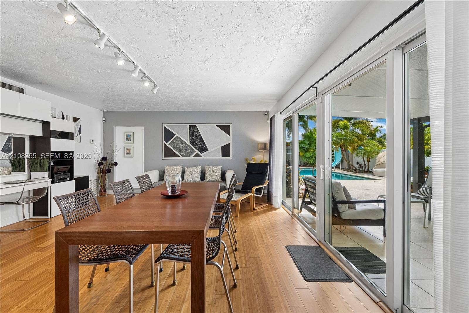 1650 NE 171st Street, North Miami Beach, North Miami Beach, FL 33162 Living area featuring wood-finish flooring, built-in cabinetry, ceiling-mounted track lighting, and expansive sliding glass doors providing access to a paved patio and outdoor swimming pool