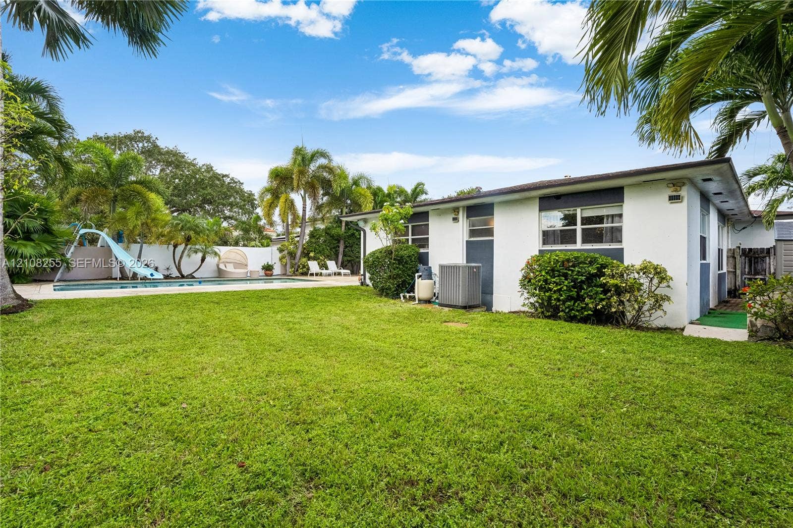 1650 NE 171st Street, North Miami Beach, North Miami Beach, FL 33162 Expansive backyard featuring a rectangular swimming pool with a slide, masonry perimeter wall, mature palm trees, and manicured lawn