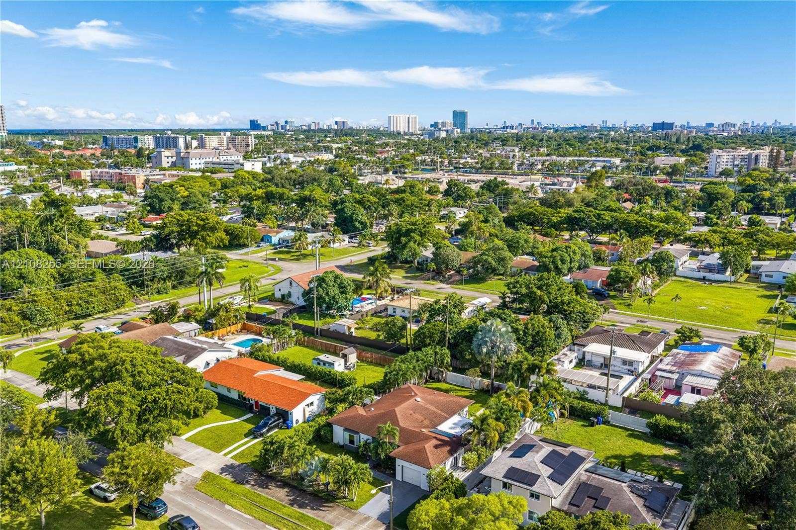 1650 NE 171st Street, North Miami Beach, North Miami Beach, FL 33162 Aerial perspective of a suburban neighborhood featuring extensive mature tree canopy, residential lots with manicured lawns, and rooftops equipped with solar energy panels