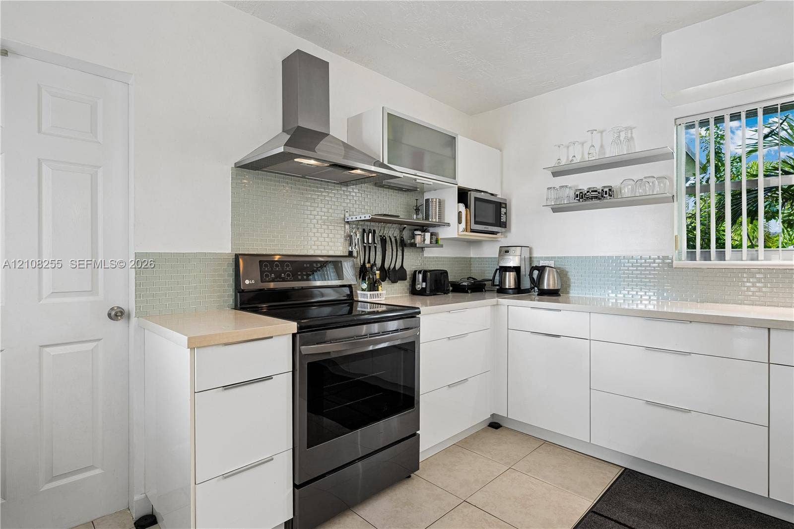 1650 NE 171st Street, North Miami Beach, North Miami Beach, FL 33162 Kitchen featuring white flat-panel cabinetry, light-colored tile backsplash, stainless steel range with overhead ventilation hood, neutral countertops, and tile flooring