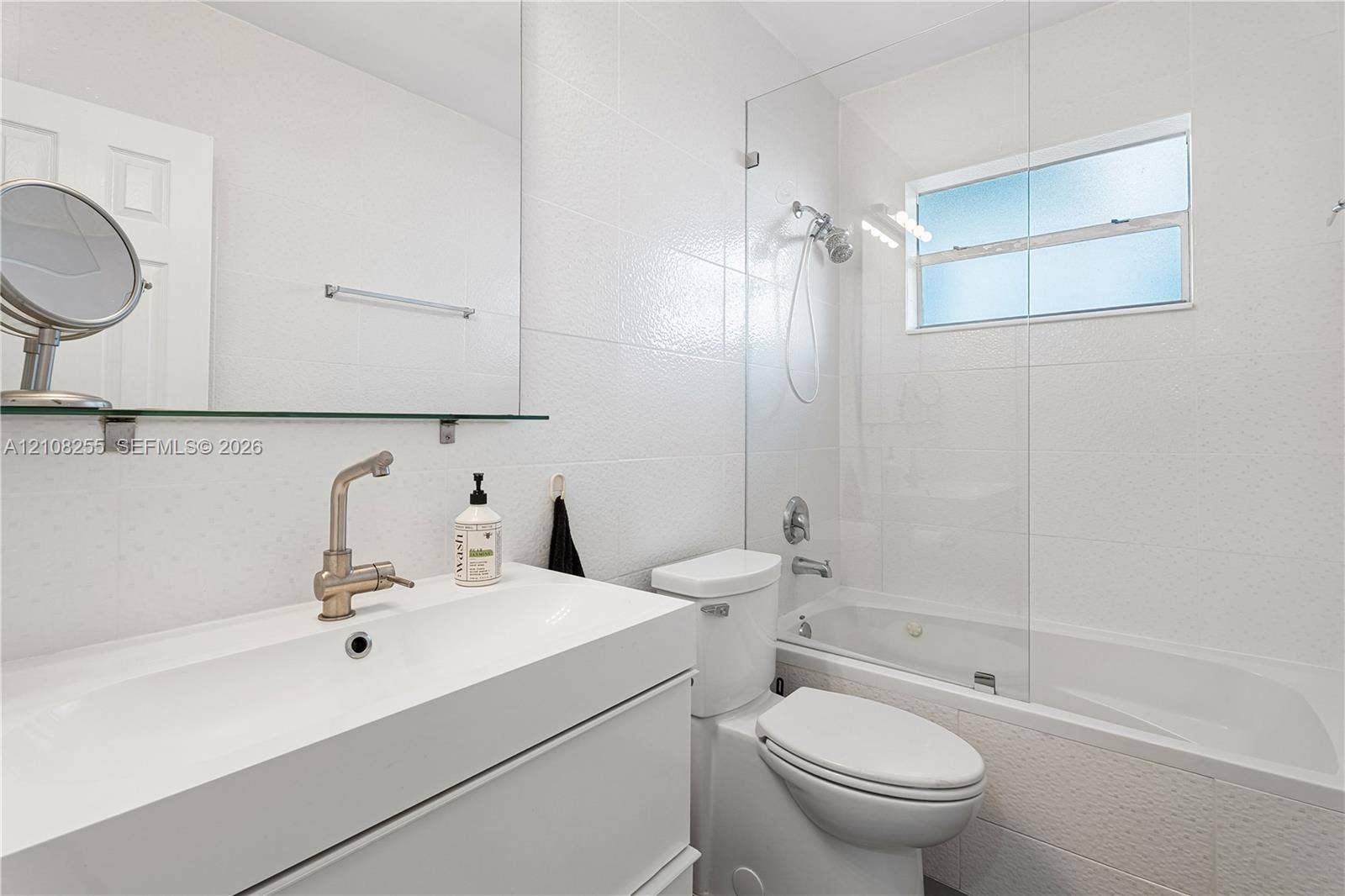 1650 NE 171st Street, North Miami Beach, North Miami Beach, FL 33162 White vanity with an integrated sink, wall-mounted mirror, glass-enclosed shower and tub combination, and brushed-finish metal faucet
