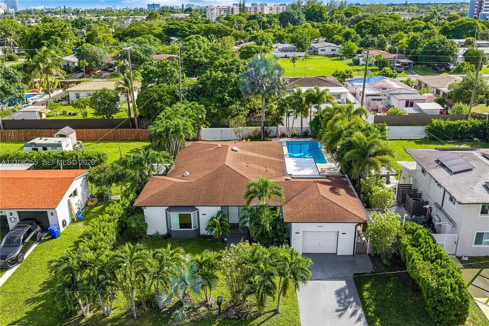 1650 NE 171st Street, North Miami Beach, North Miami Beach, FL 33162 Single-story residence featuring a hipped roof, attached garage, bay window, and a rear swimming pool set within a manicured landscape