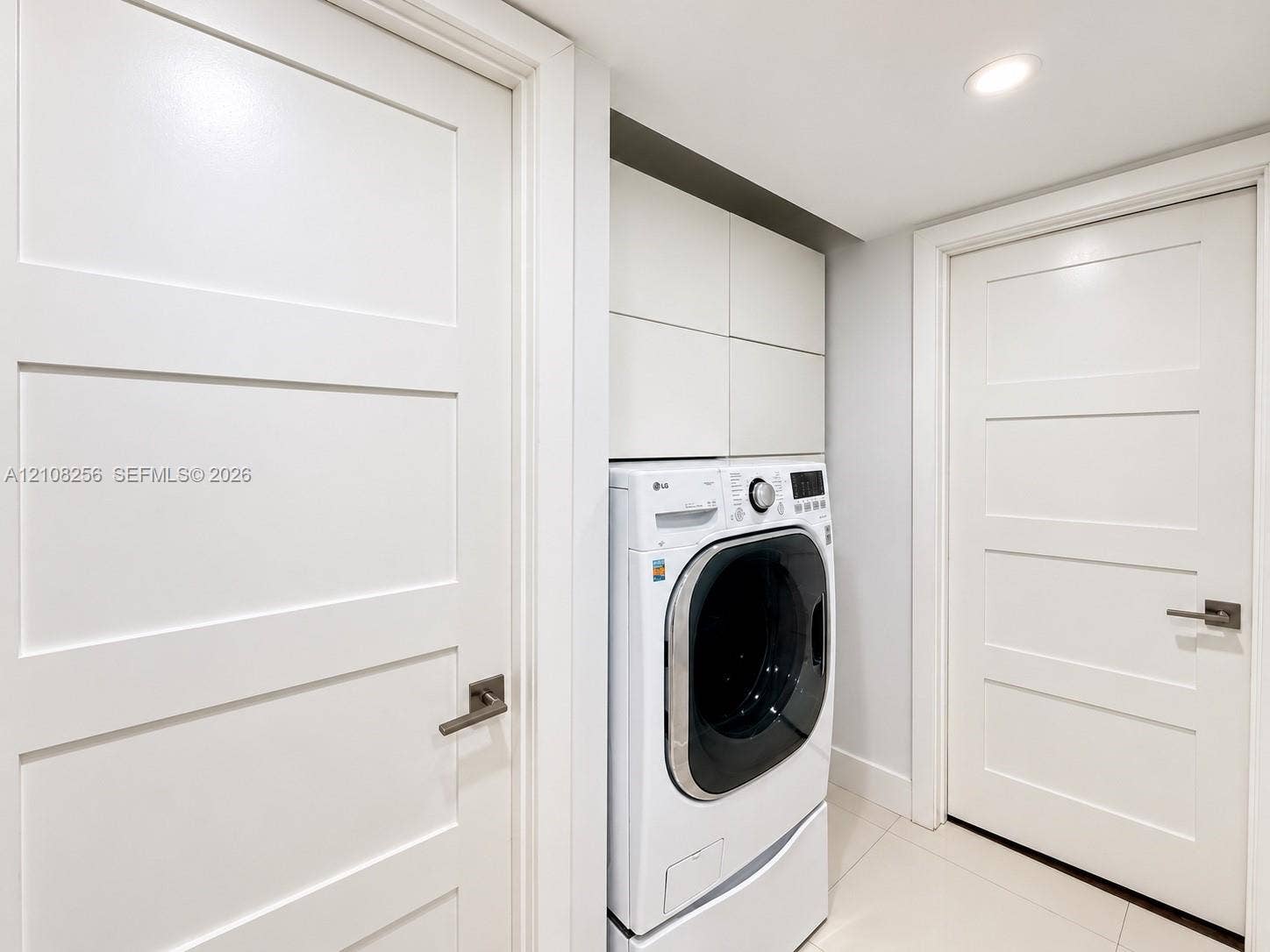 9350 Fontainebleau Boulevard, #110, Miami, Miami, FL 33172 Laundry area featuring built-in cabinetry, recessed lighting, and tile flooring, framed by two white Shaker-style doors with metallic lever handles