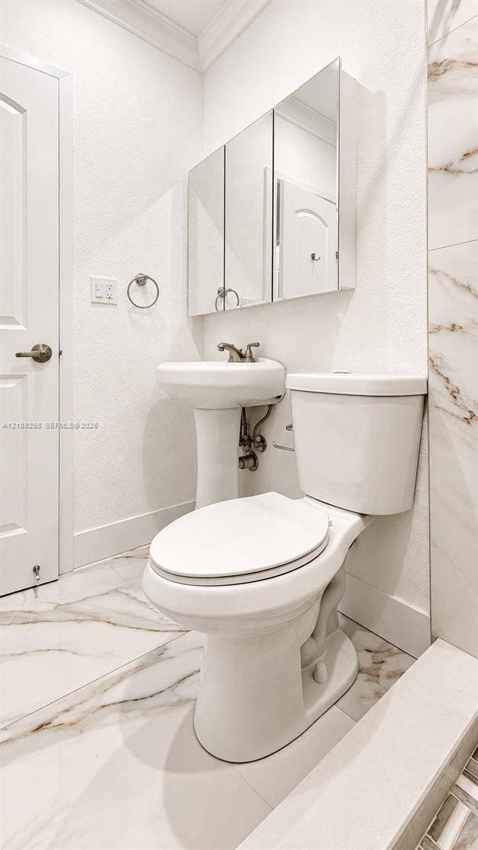 909 NE 111th Street, #909, Biscayne Park, Biscayne Park, FL 33161 Pedestal sink with metallic faucet, multi-panel mirrored medicine cabinet, elongated toilet, and large-format tile flooring with veined detailing