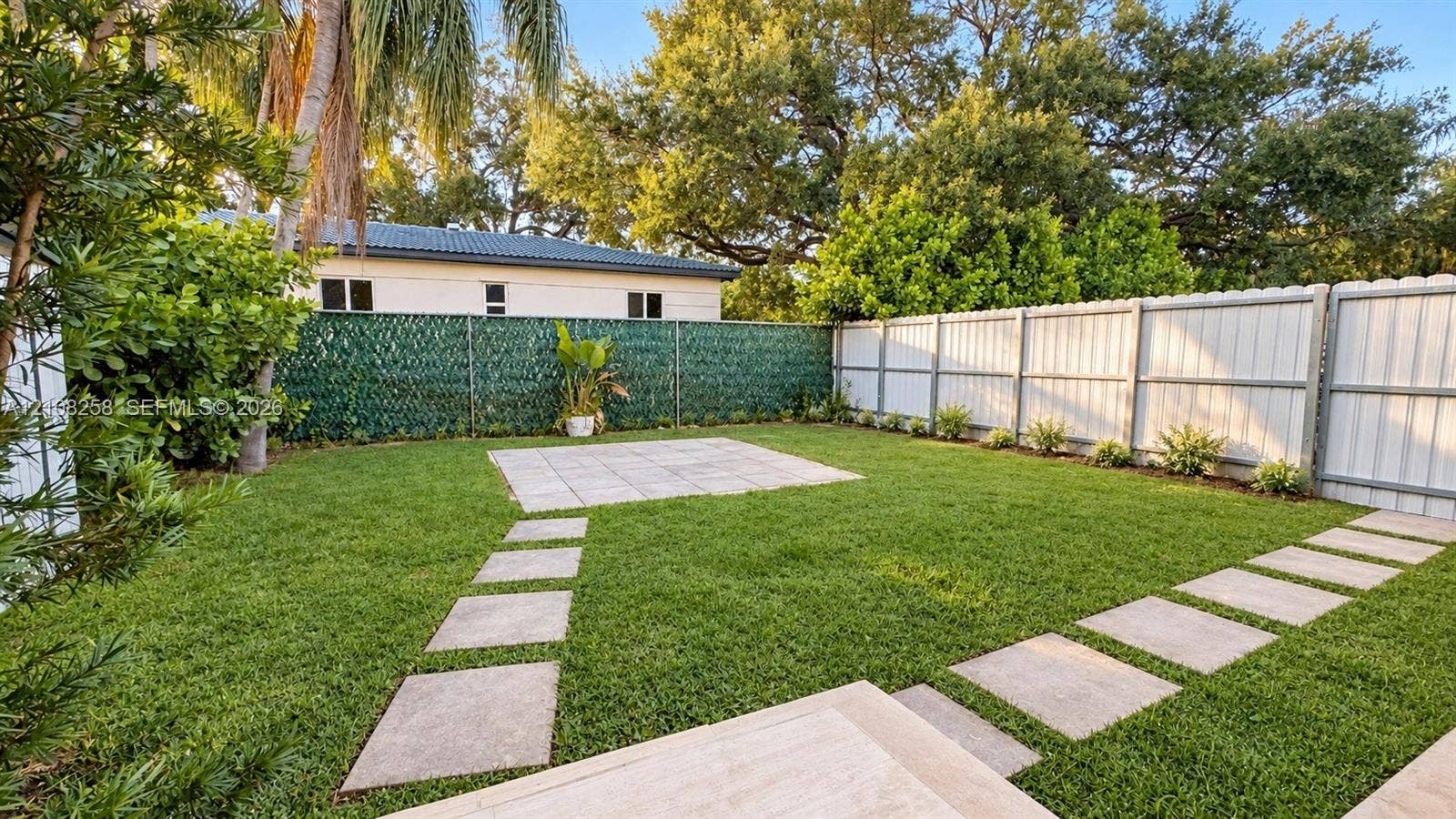 909 NE 111th Street, #909, Biscayne Park, Biscayne Park, FL 33161 Backyard featuring a manicured lawn, stone paver walkways, a centralized stone patio, and perimeter fencing