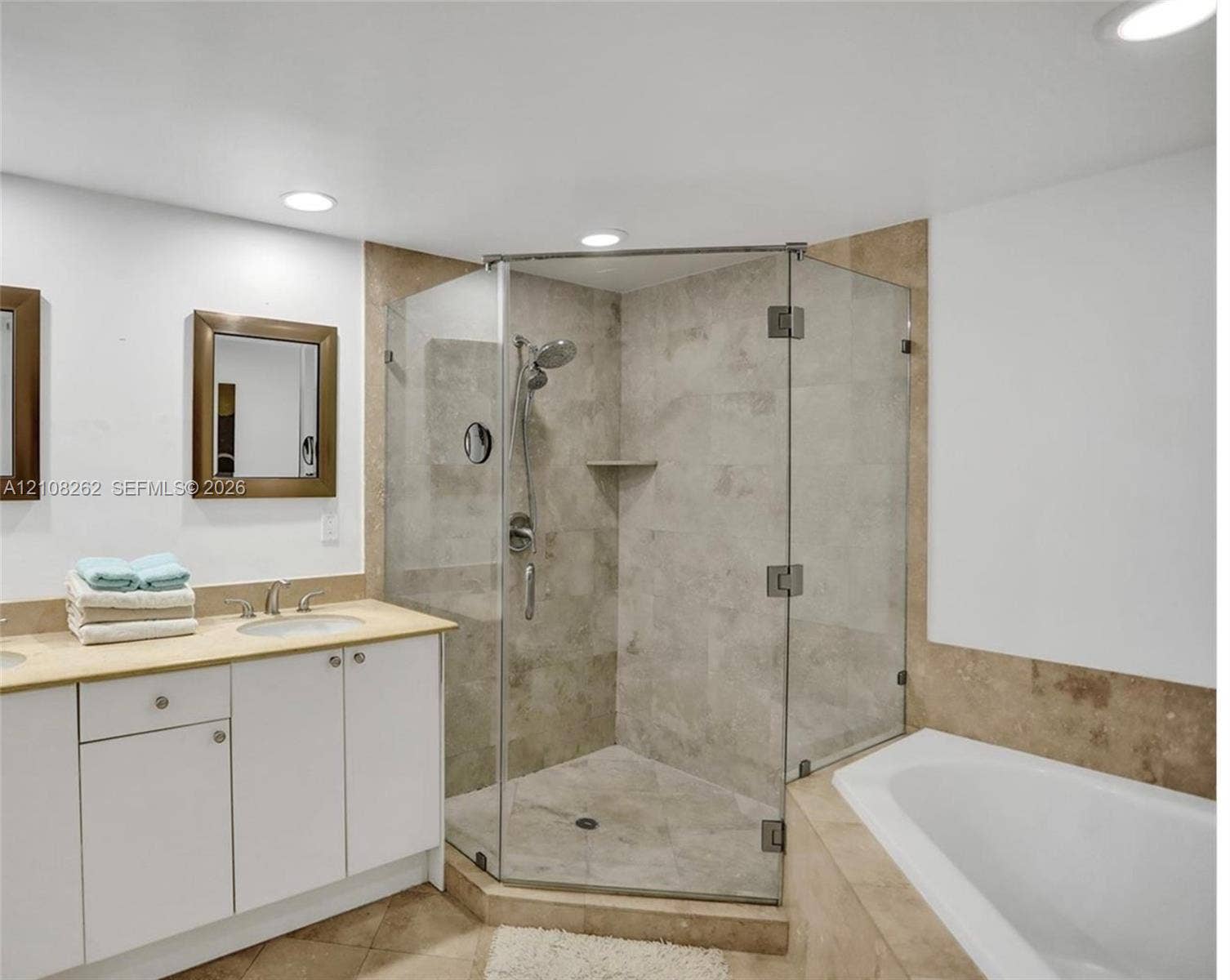 Corner glass-enclosed shower with tile surround, built-in soaking tub, stone-topped vanity with undermount sink, and recessed lighting