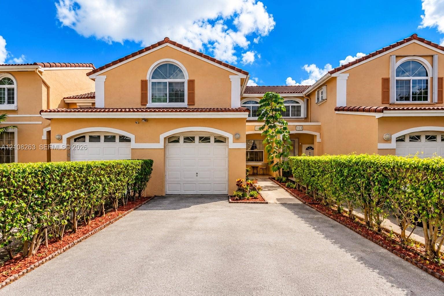 14817 Balgowan Road, #102-5, Miami Lakes, FL 33016 Stucco exterior featuring arched garage entryways, decorative shutters, clay tile roofing, and manicured privacy hedging