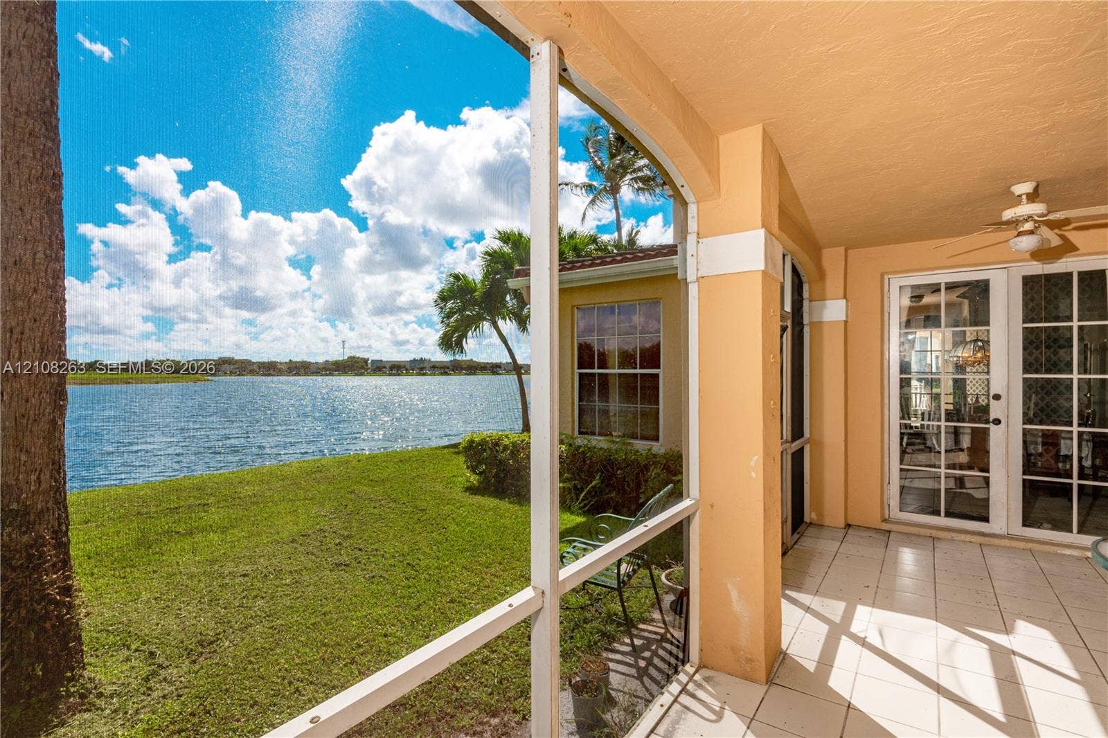 14817 Balgowan Road, #102-5, Miami Lakes, FL 33016 Covered screened-in patio featuring tile flooring, a ceiling fan, and sliding glass door access, overlooking a waterfront lawn