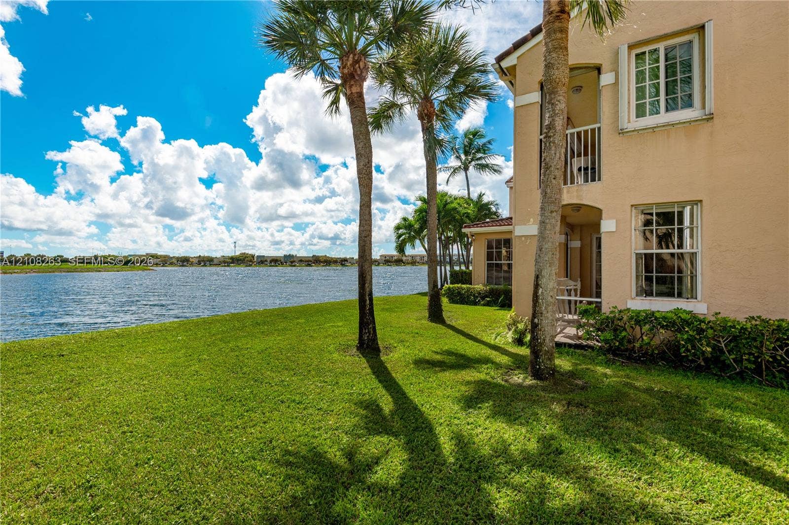 14817 Balgowan Road, #102-5, Miami Lakes, FL 33016 Multi-story exterior featuring a stucco facade, second-story balcony, ground-level covered patio, and immediate water frontage