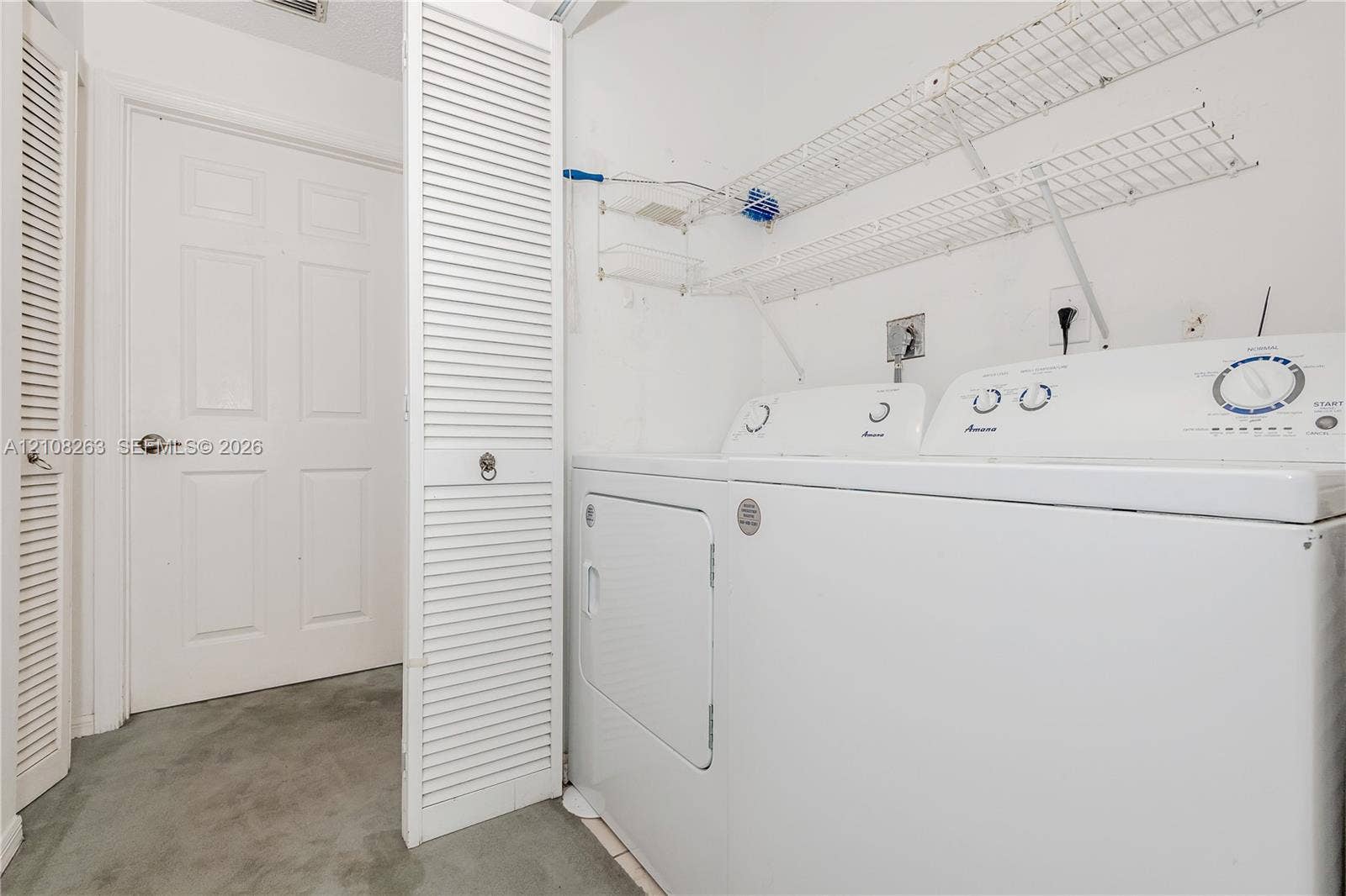 14817 Balgowan Road, #102-5, Miami Lakes, FL 33016 Laundry area featuring louvered bi-fold closet doors, wall-mounted wire shelving, and a paneled interior door