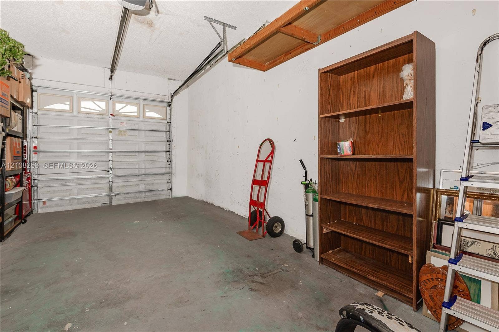 14817 Balgowan Road, #102-5, Miami Lakes, FL 33016 Garage space featuring an overhead sectional garage door with inset windows, concrete flooring, and mounted overhead storage shelving