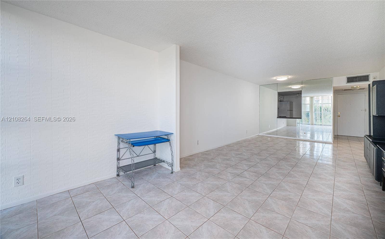 Open-concept area featuring light-toned tile flooring, floor-to-ceiling mirrored wall paneling, and flush-mount ceiling lighting
