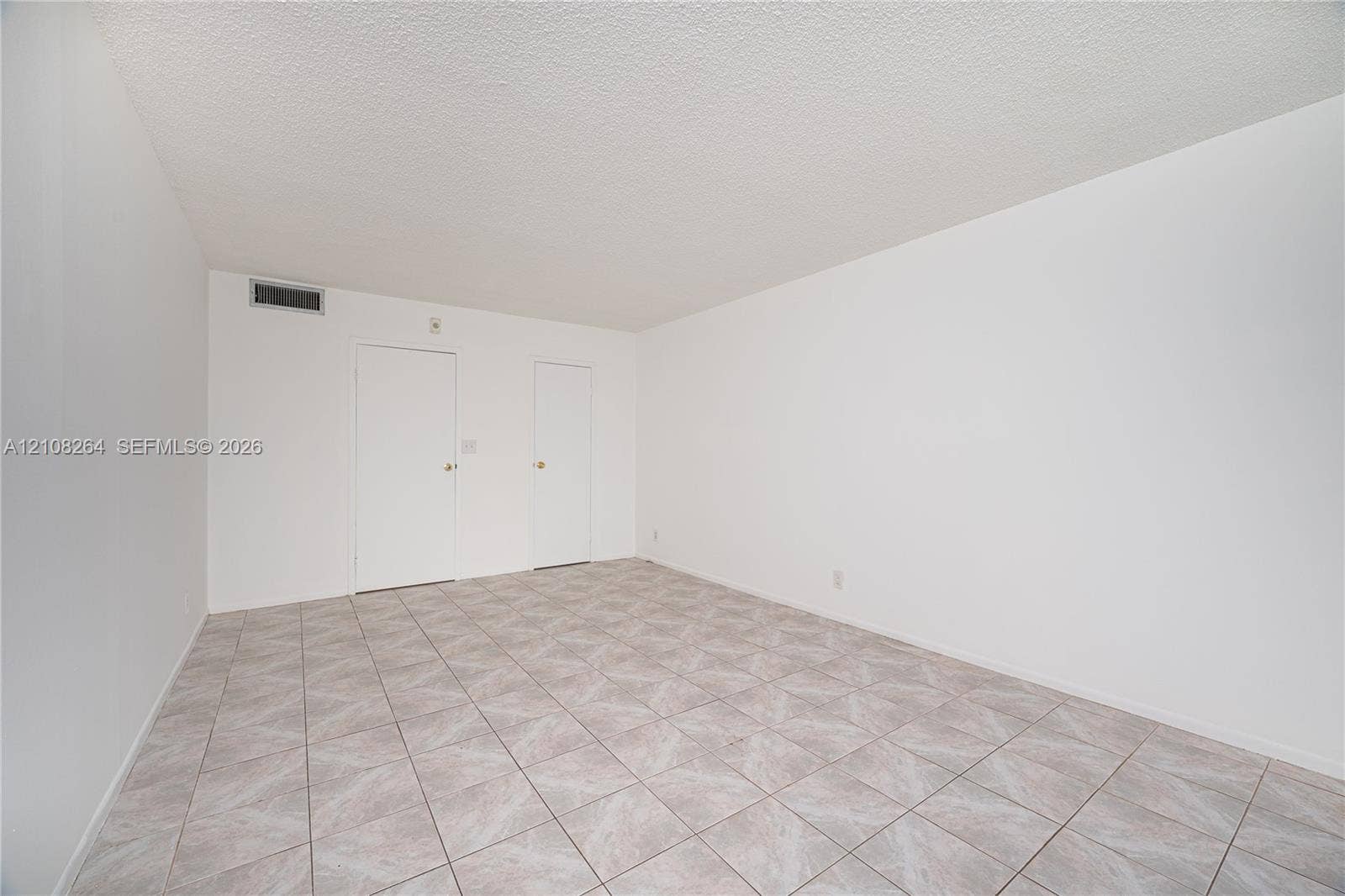 Neutral-toned tile flooring, textured ceiling, and dual interior doors finished in white