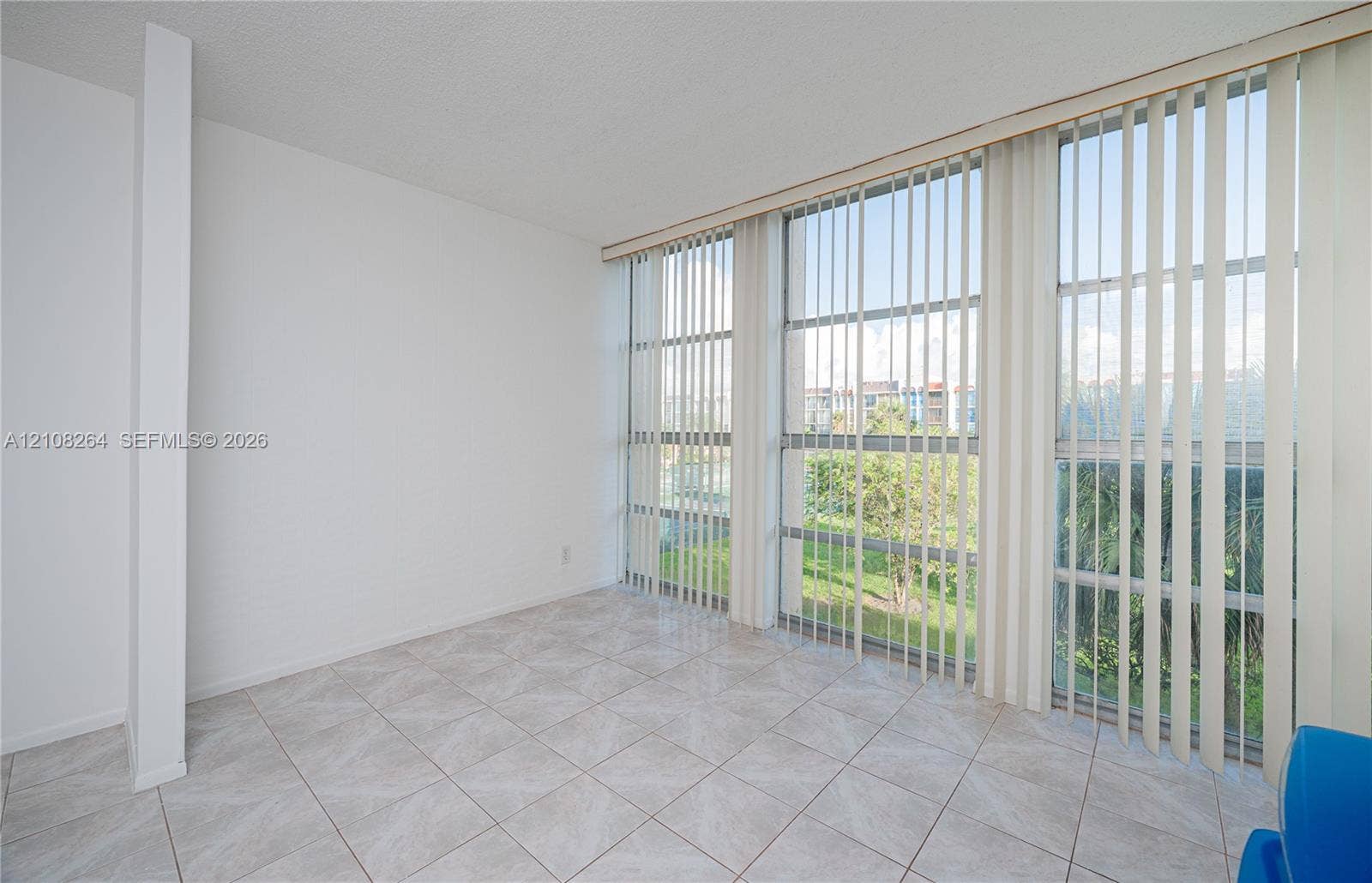 Interior space featuring neutral tile flooring, expansive floor-to-ceiling windows, and vertical blinds