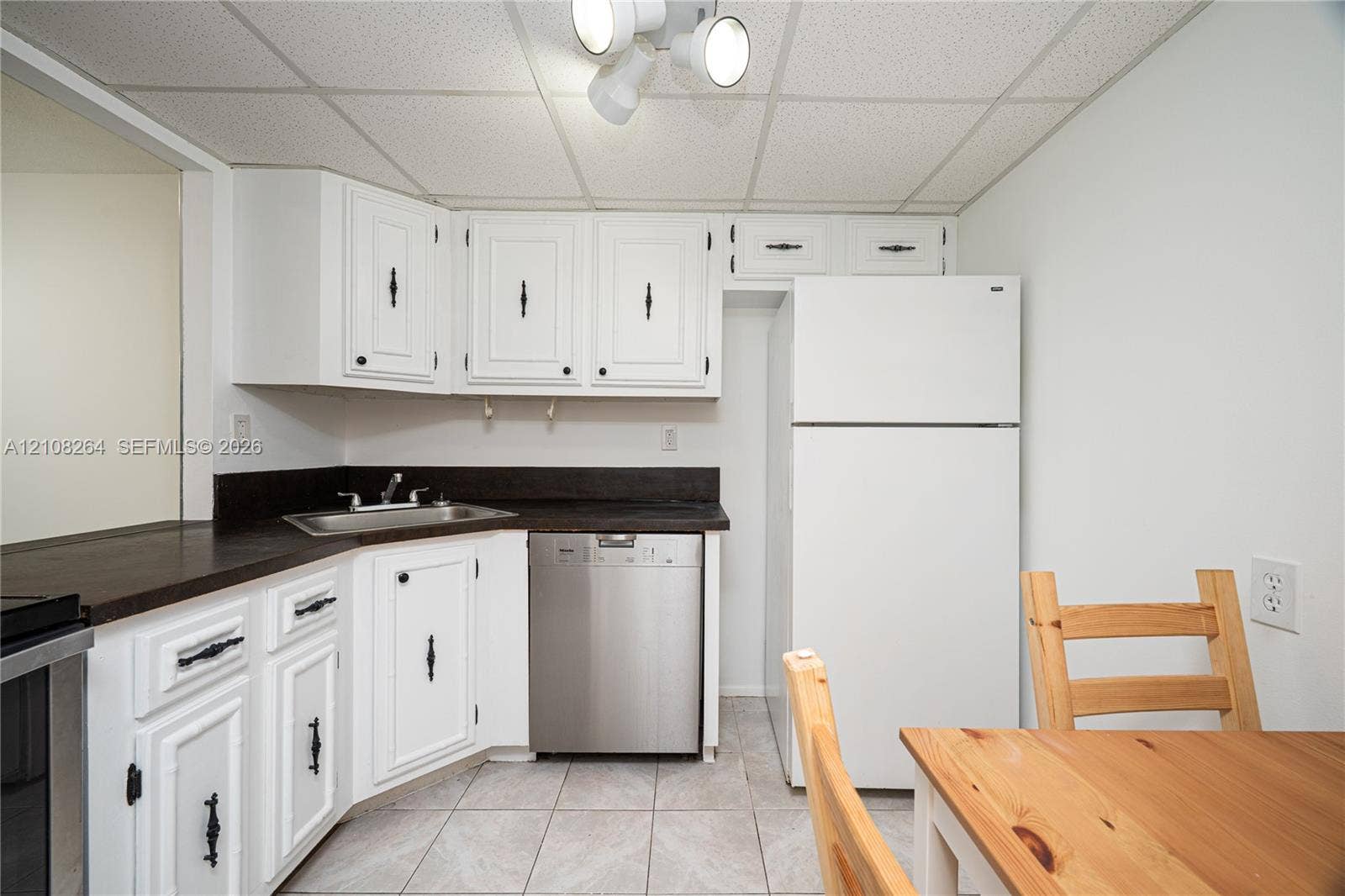 Kitchen featuring white cabinetry with dark hardware, dark countertops, a stainless steel dishwasher, and tile flooring