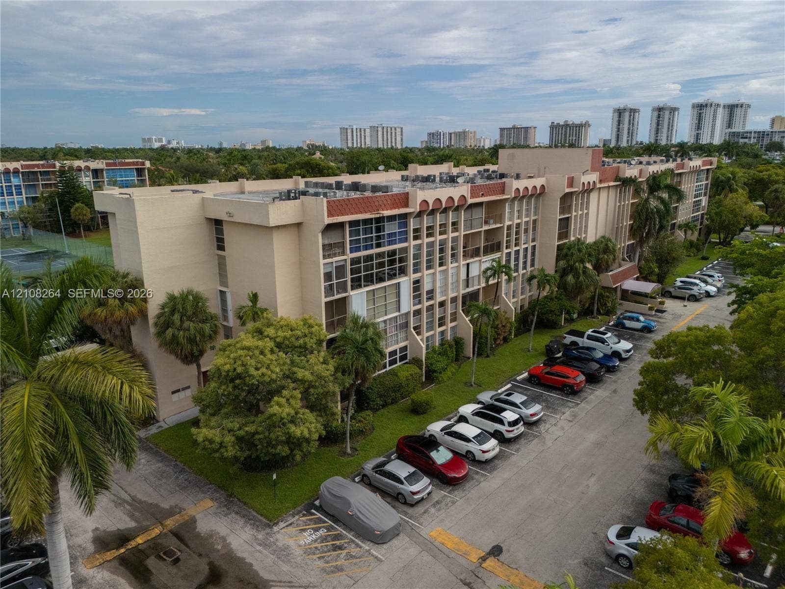 Multi-story architectural exterior featuring recessed balconies, concrete facade, flat roofline, and mature landscaping