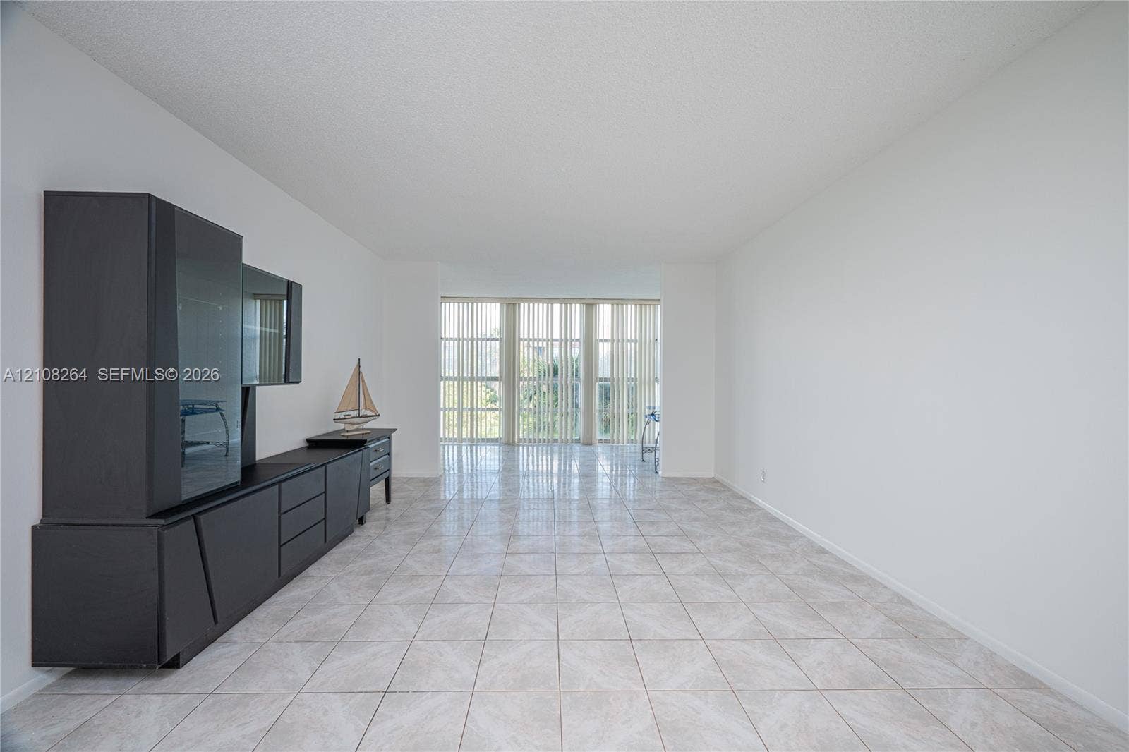 Open-concept living space featuring neutral ceramic tile flooring, floor-to-ceiling windows, and vertical blinds