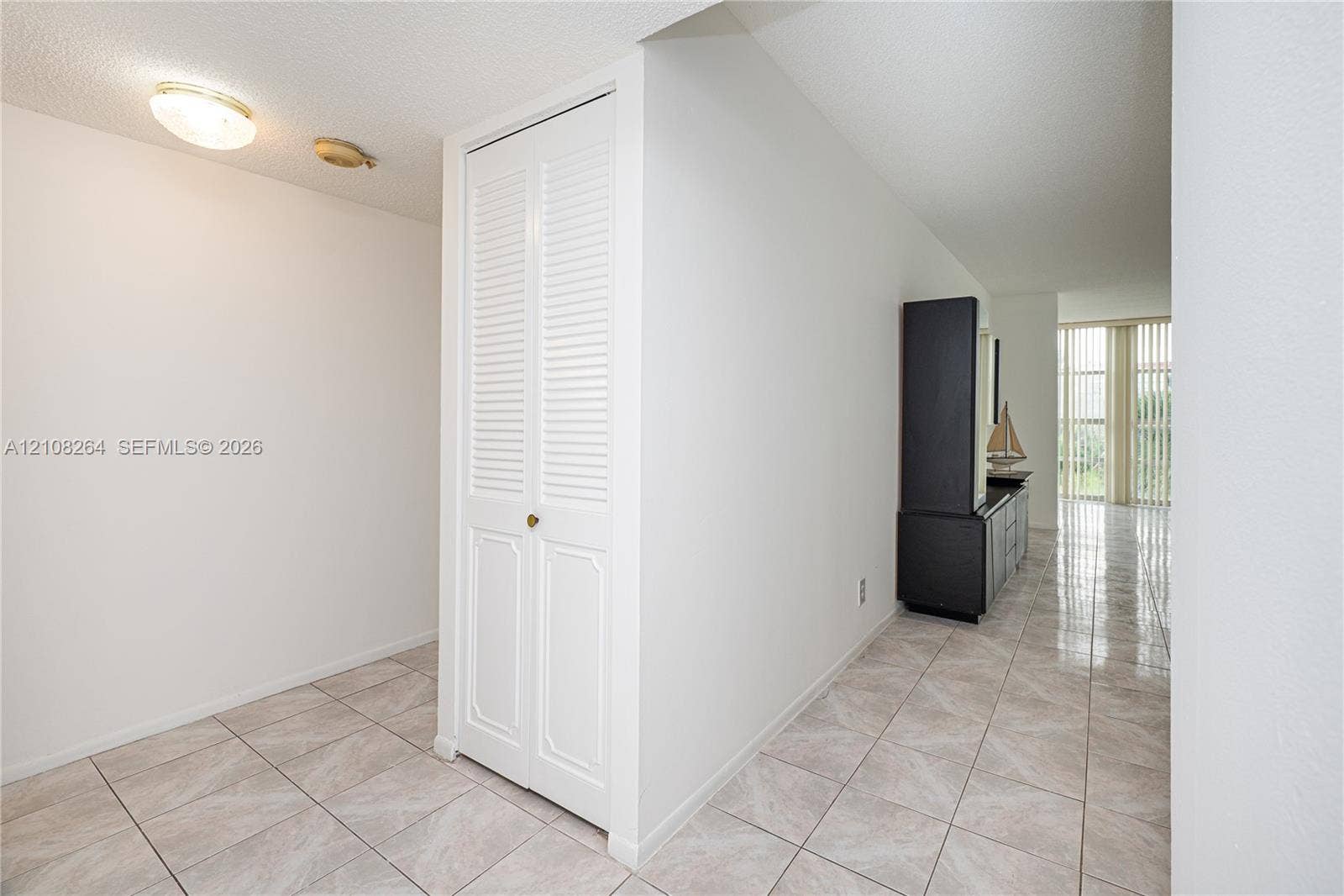 Neutral ceramic tile flooring, white louvered-panel closet doors, and floor-to-ceiling vertical blinds