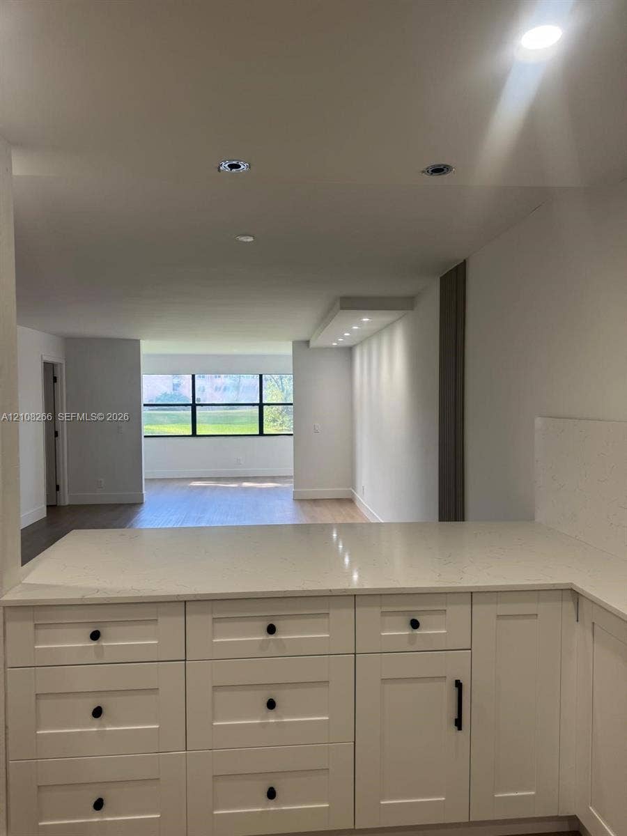 9721 Sunrise Lakes Boulevard, #108, Sunrise, FL 33322 White Shaker-style cabinetry featuring matte black hardware, stone-finish countertops, recessed ceiling lighting, and wood-finish flooring