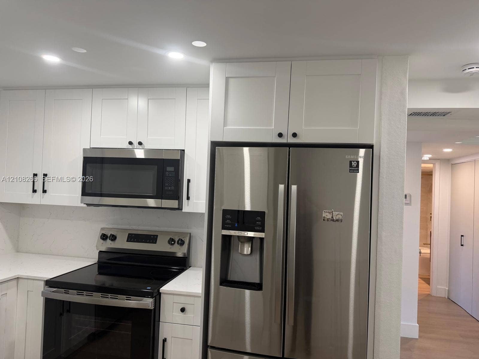 9721 Sunrise Lakes Boulevard, #108, Sunrise, FL 33322 White shaker-style cabinetry with matte black hardware, stone-finish countertops, stainless steel side-by-side refrigerator, built-in stainless steel microwave, and recessed lighting